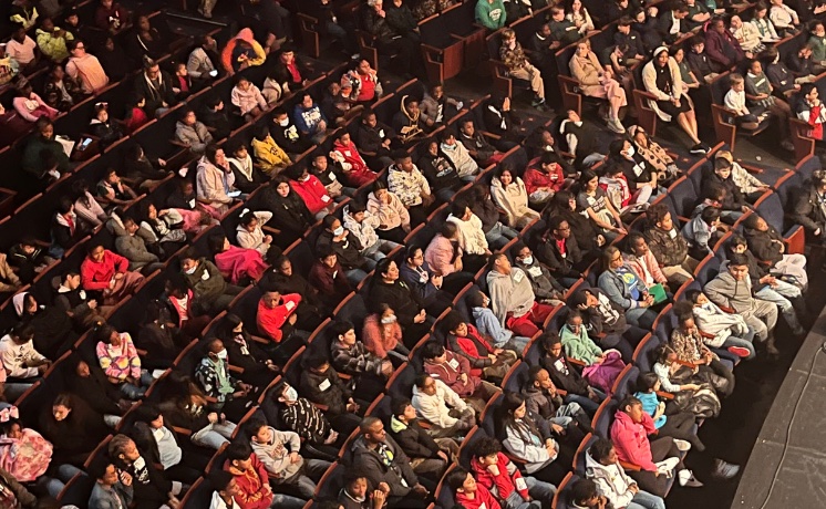 children seated in a performance hall viewed from above