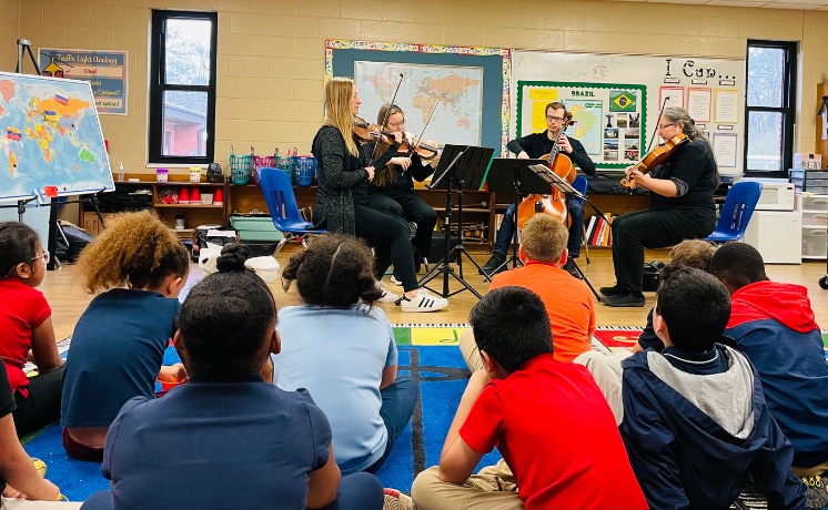 string quartet performing for children who are seated on the floor with their backs to the viewer