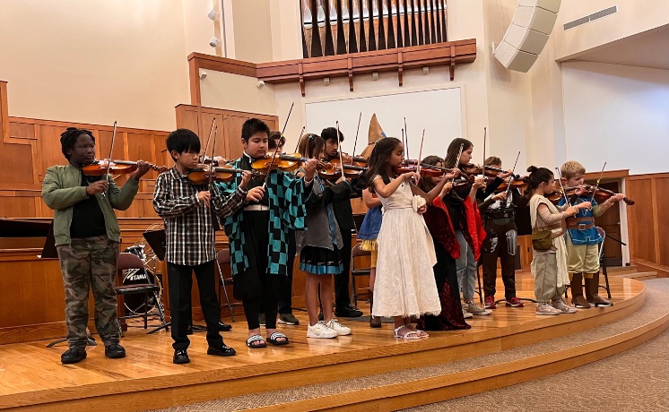 student violinists on a wood-floored stage