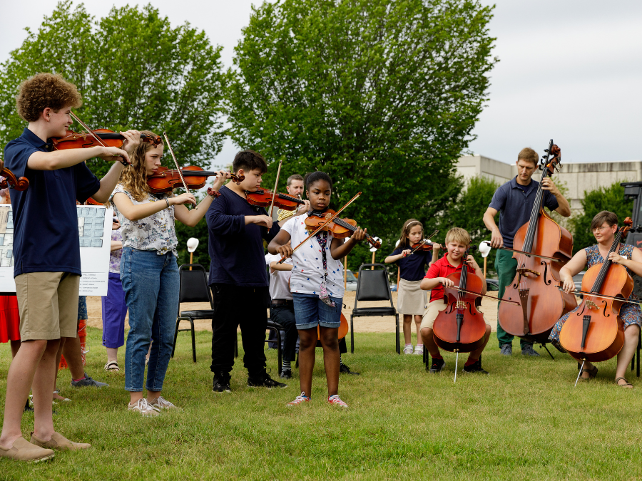 kids playing stringed instruments outside with trees in the background