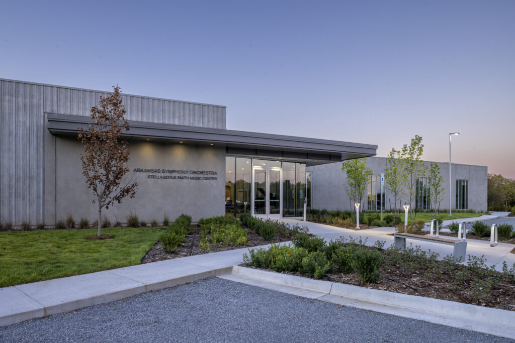 A modern, single-story building with a glass entrance and landscaped grounds; the sign reads ASO Music Center—Arkansas Symphony Orchestra Stella Boyle Smith Music Center.