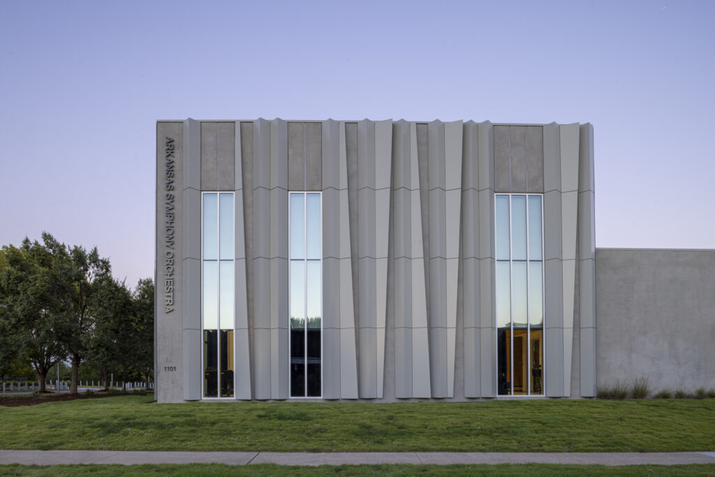 Modern building with vertical concrete panels, tall narrow windows, and ASO Music Center sign on the left side, set against a clear sky and grassy lawn.