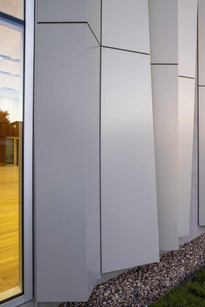 Close-up of the ASO Music Centers modern facade, featuring large, angled gray panels and a glass window on the left, with rocks at the base.
