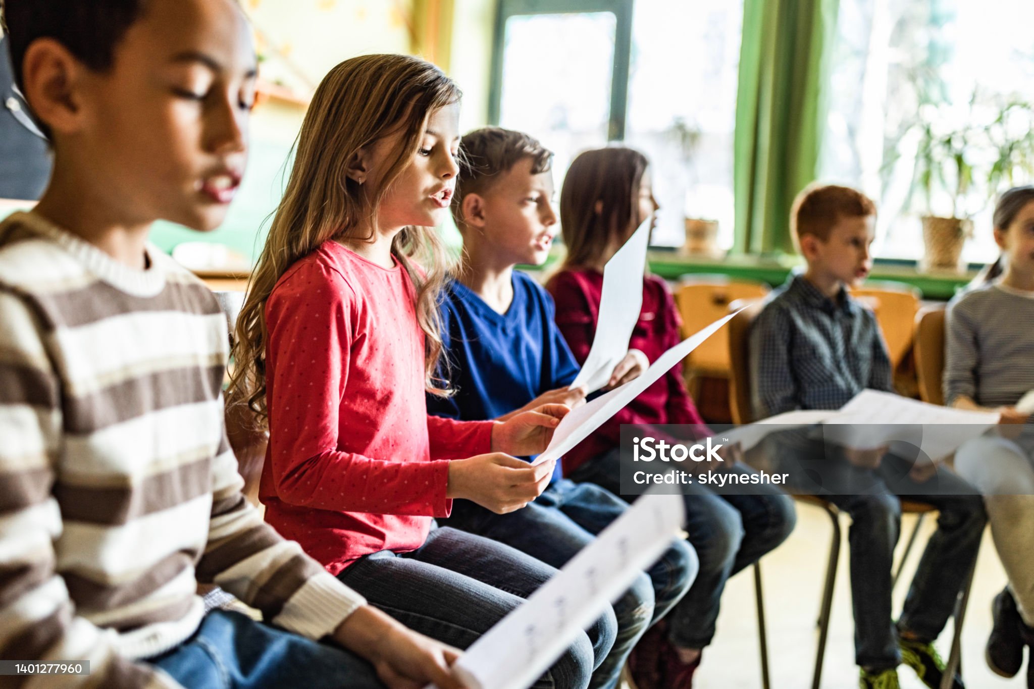 Large group of elementary students singing on a music class at school. Focus is on girl.