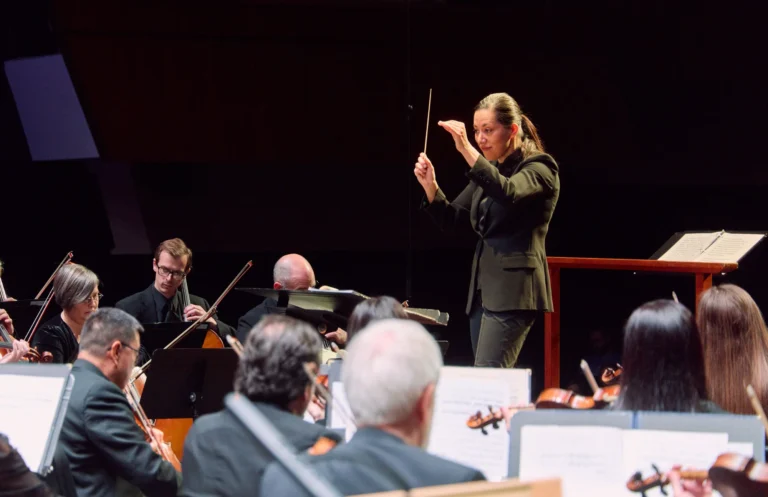 A conductor leads the Arkansas Symphony Orchestra during a performance, with musicians playing string instruments